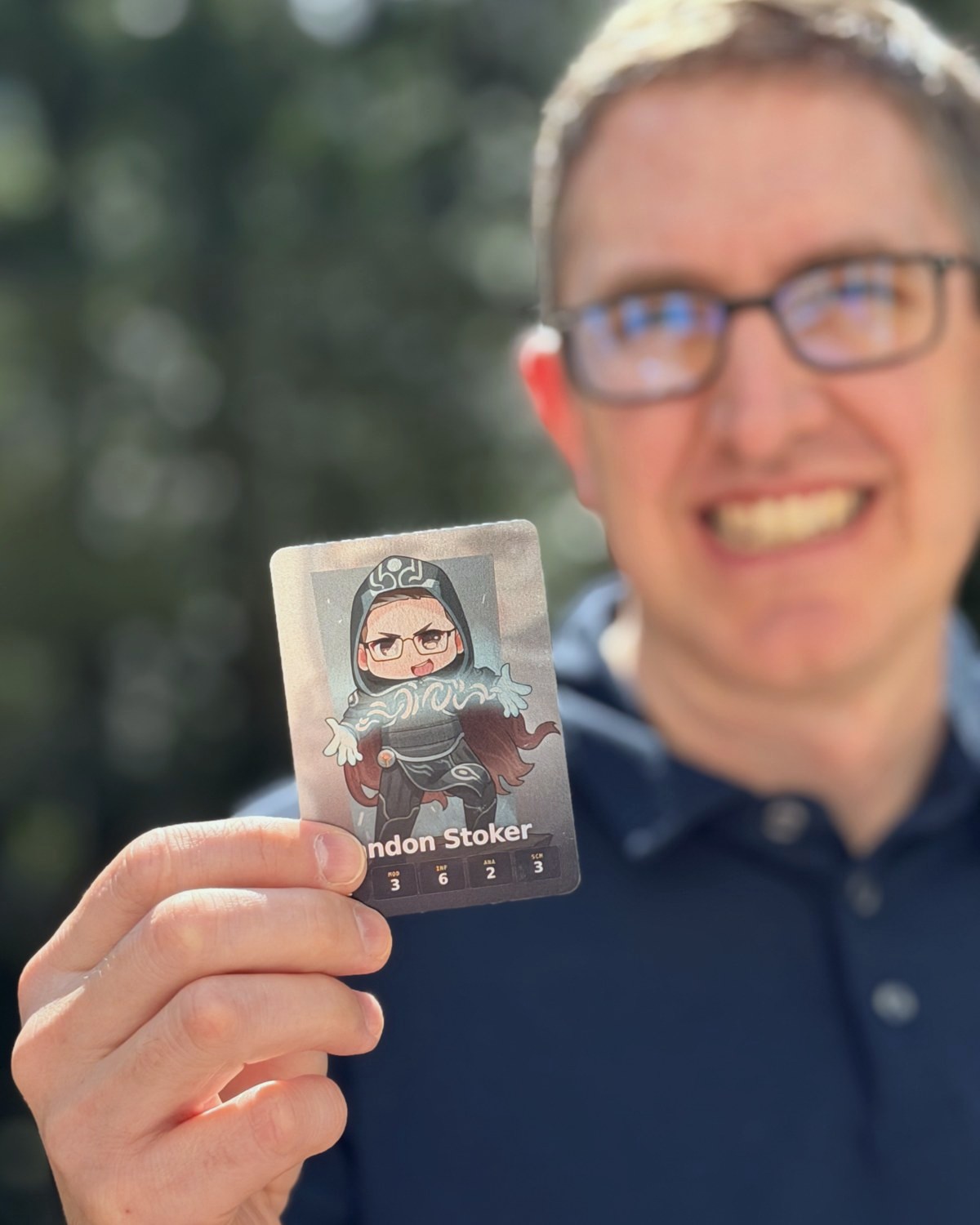 Close-up of a Deck of Us card held in hand, showing the chibi art and stat line.